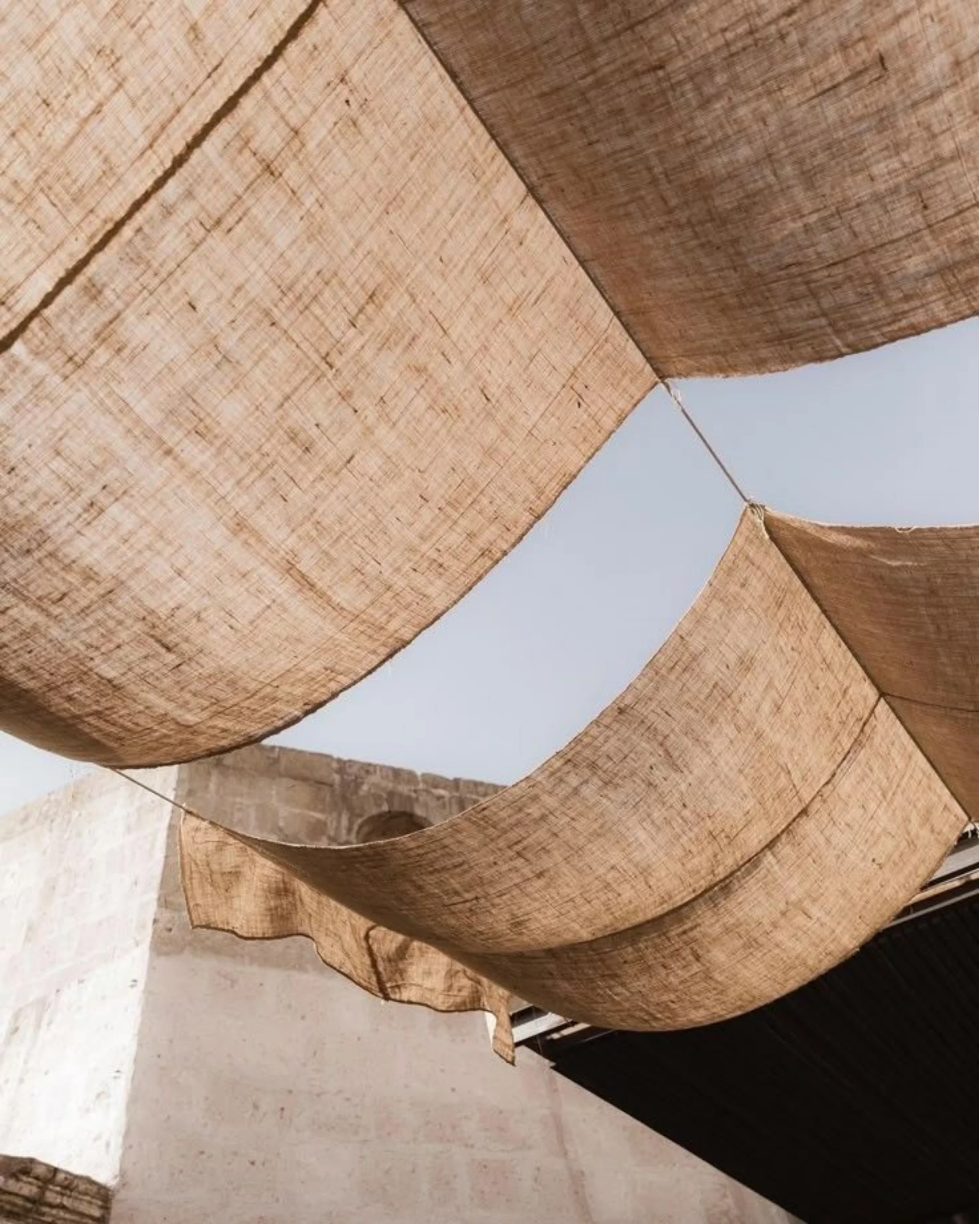 Natural fabric canopies suspended above a sunlit courtyard